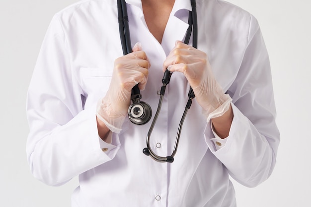 Vista recortada do jovem médico feminino segurando o estetoscópio pendurado no pescoço, estúdio tiro sobre parede branca