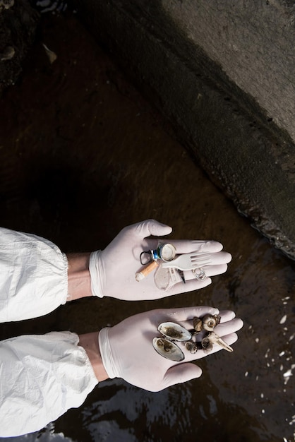 Vista recortada de ecologista en guantes de látex con conchas marinas y basura plástica