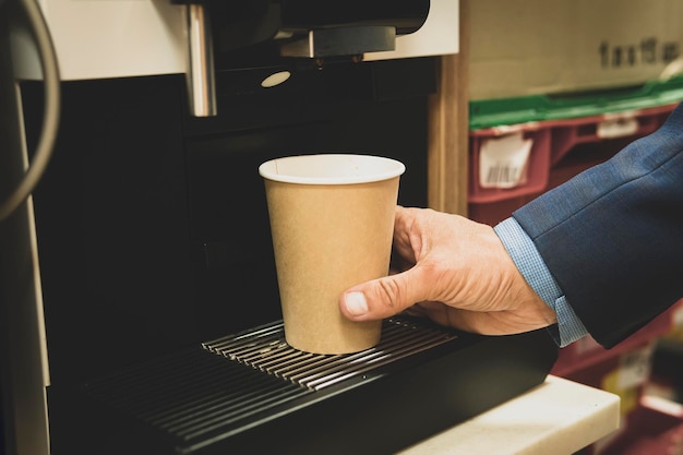 Vista recortada del empresario presionando el botón de la cafetera mientras prepara el café para llevar. El hombre toma café de una máquina expendedora