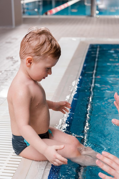 Vista recortada del entrenador de natación cerca de un niño pequeño lindo en la piscina