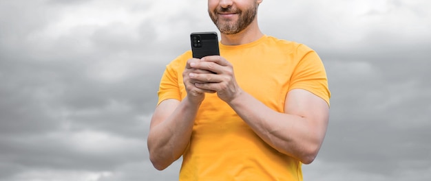 Foto vista recortada del hombre chateando en el teléfono inteligente en el fondo del cielo