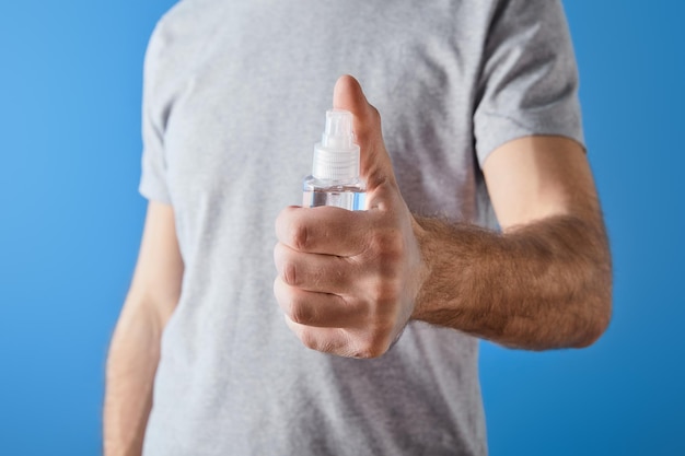 Vista recortada del hombre que sostiene el desinfectante de manos en gel en botella aislado en azul