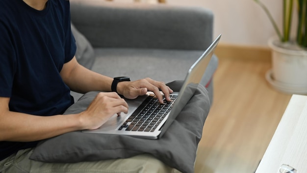 Vista recortada del hombre sentado en el sofá y trabajando en línea o navegando por Internet con una computadora portátil