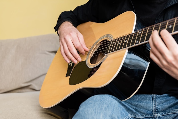 Vista recortada del hombre tocando la guitarra acústica en el sofá en casa