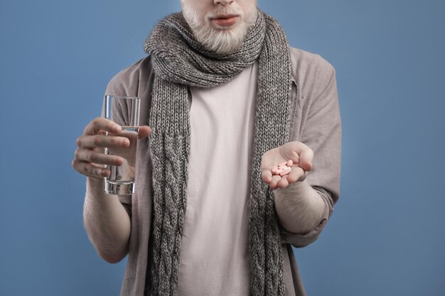 Vista recortada del hombre tomando pastillas sosteniendo un vaso de agua dulce en el fondo azul del estudio recortado
