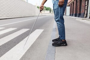 Foto vista recortada de un joven negro con discapacidad visual parado en la carretera usando bastón para caminar