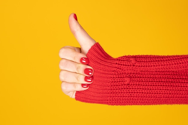 Vista recortada de la mano femenina en suéter rojo que muestra el pulgar hacia arriba aislado en amarillo