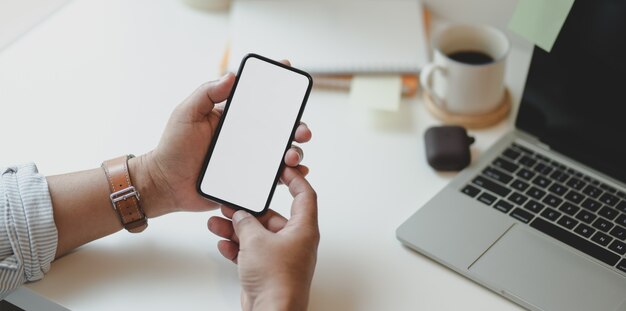 Vista recortada de la mano del hombre que sostiene el teléfono inteligente de pantalla en blanco