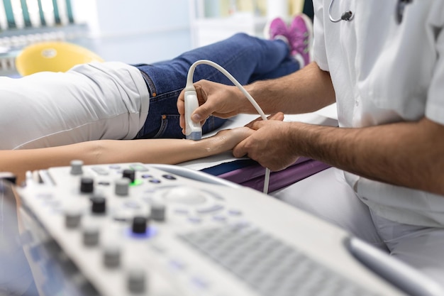 Vista recortada del médico masculino que sostiene un dispositivo especial mientras realiza la terapia de ultrasonido para la mujer Concepto de ultrasonido de las venas de las extremidades superiores