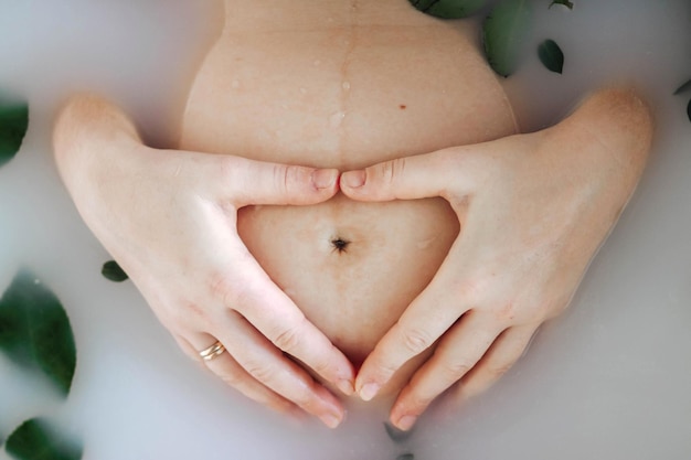 Vista recortada de la mujer embarazada bañándose con flores y leche