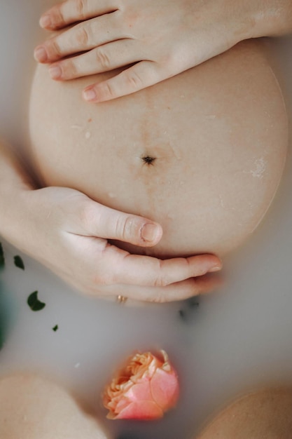 Vista recortada de la mujer embarazada bañándose con flores y leche