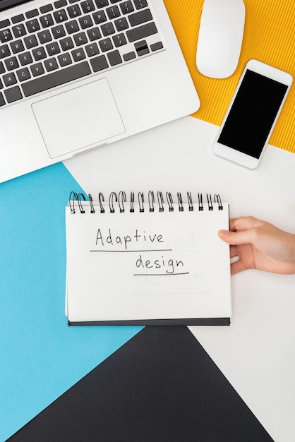 Foto vista recortada de la mujer que sostiene el cuaderno con letras de diseño adaptativo cerca del teléfono inteligente portátil