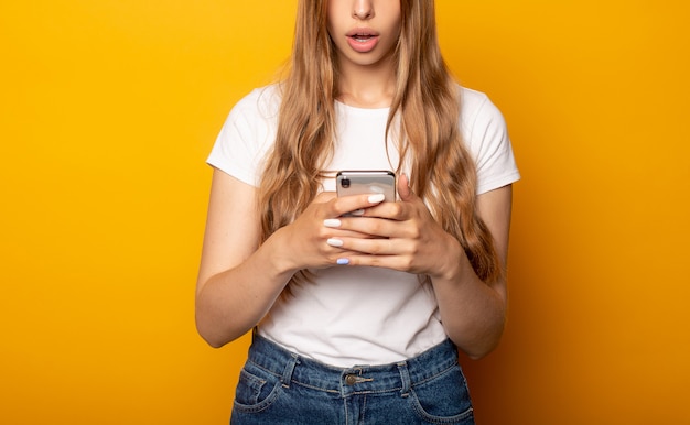 Vista recortada de niña sorprendida con smartphone aislado en amarillo