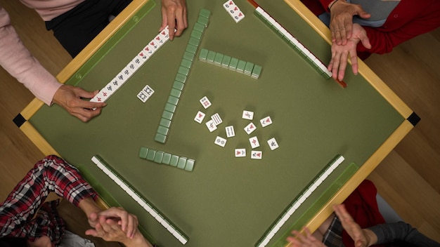 Foto vista recortada no topo de todos batendo palmas para o pai enquanto ele reivindica o tile coringa descartado pelo último jogador e mostrando seu conjunto completo na mesa de mahjong verde