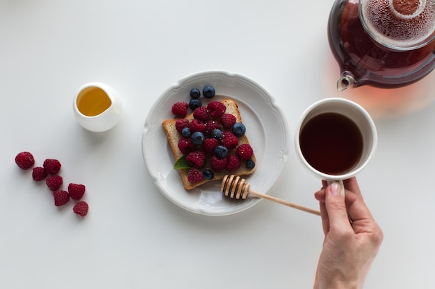 Vista recortada de la persona con té y tostadas con arándanos y frambuesas para el desayuno aislado