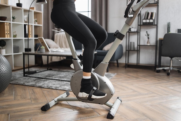 Vista recortada de las piernas de la atleta femenina usando ropa deportiva y usando bicicleta de ejercicio