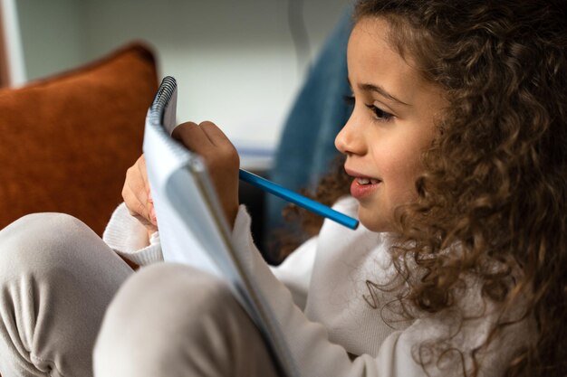 Foto vista recortada del retrato del niño multirracial sosteniendo un cuaderno y escribiendo mientras estudiaba en casa de forma remota foto de archivo