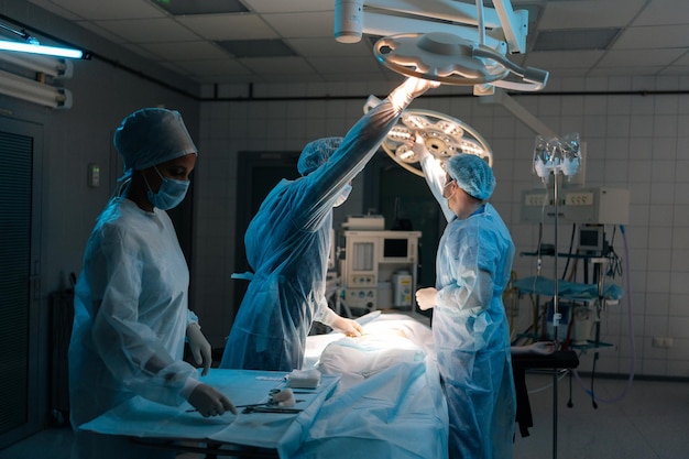 Vista remota del médico con uniformes quirúrgicos y máscaras ajustando la luz antes de la operación en la operación