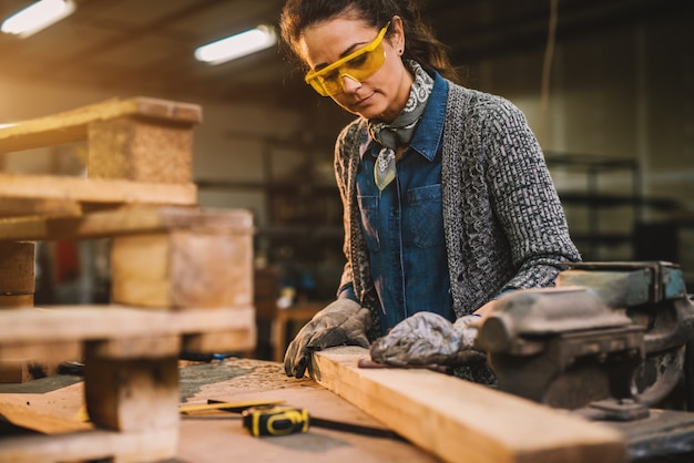 Vista de retrato de feliz atractivo profesional femenino carpintero trabajador mirando y eligiendo madera en el taller