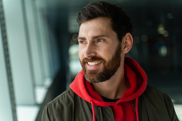 Vista de retrato del joven hombre barbudo caucásico mirando hacia otro lado mientras está de pie en el aeropuerto. Se siente genial antes de su viaje.