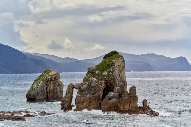 Vista de rocas en la orilla del mar mientras las olas rompen en un día nublado