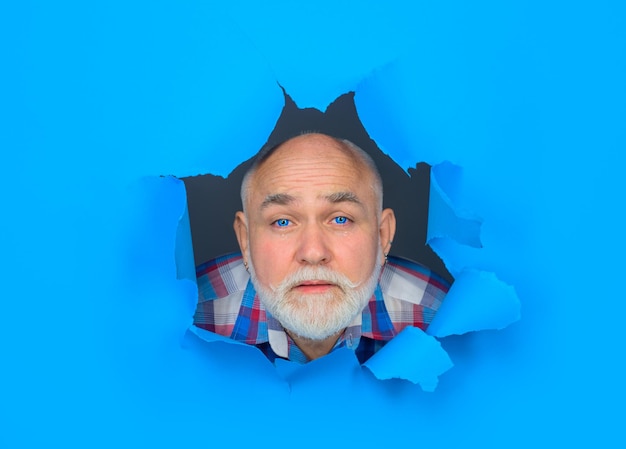 Vista del rostro masculino a través del orificio en papel azul llorando barbudo a través del orificio en el espacio de copia de papel para