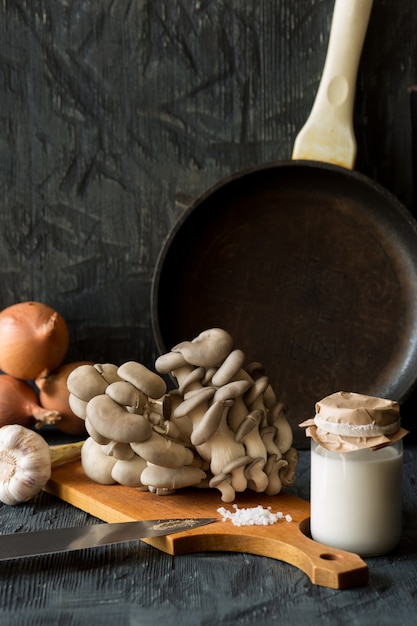 Vista de setas ostra frescas con crema, especias, hierbas y verduras sobre fondo de madera oscura.