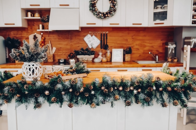 Vista sobre a bela cozinha branca com decorações de natal em todos os armários e placa da cozinha. há uma guirlanda de natal no armário. galhos de árvores de abeto naturais com pinhas.