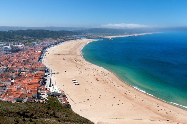 Vista sobre la costa de playa de arena con mar, luz solar, cielo azul en Nazare, Portugal