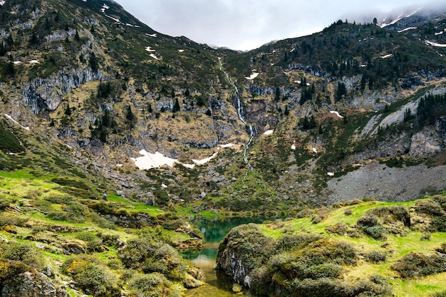 Vista sobre el hermoso lago azul de Ayes, con una cascada, los pastos y los picos en Francia