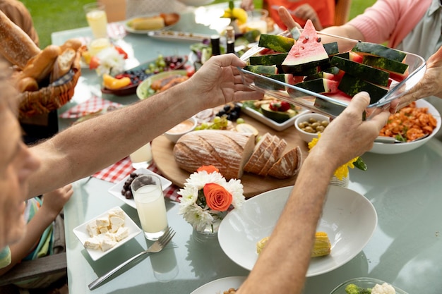 Vista sobre el hombro de una familia caucásica multigeneracional sentada afuera en una mesa para cenar, comiendo y sirviendo comida. Familia disfrutando del tiempo en casa, concepto de estilo de vida