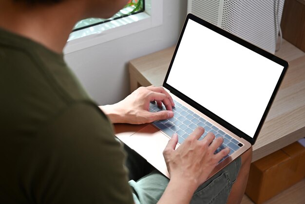 Vista sobre el hombro del joven usando una computadora portátil mientras se sienta en la sala de estar