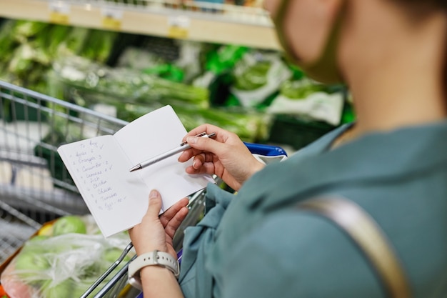 Foto vista sobre el hombro de la mujer marcando posiciones de la lista de compras con un bolígrafo mientras compra productos en el supermercado