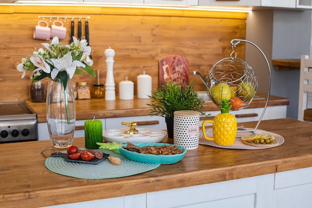 Vista sobre el mostrador de madera con bocadillos, flores de lirio, fruta fresca en la canasta, tetera y bandeja de huevos para la celebración de la Pascua.