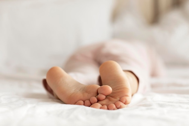 Vista sobre los pies descalzos del niño en la cama blanca Dormitorio iluminado con luz matutina Niño duerme en pijama comodidad