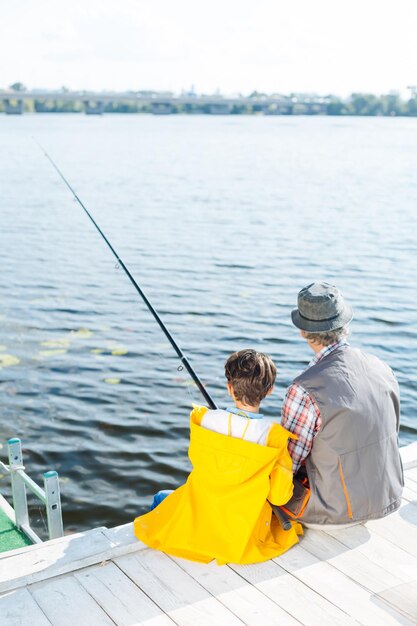 Vista superior del abuelo y el nieto sentados cerca del río y pescando el fin de semana