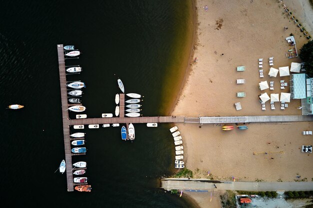 Vista superior aérea de botes y pequeños yates cerca del muelle de madera en el entretenimiento de verano del lago en el agua