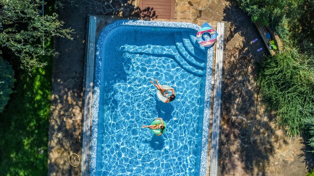 Vista superior aérea das crianças na piscina de cima, crianças felizes nadam em anéis de espuma inflável e se divertem na água em férias em família no resort