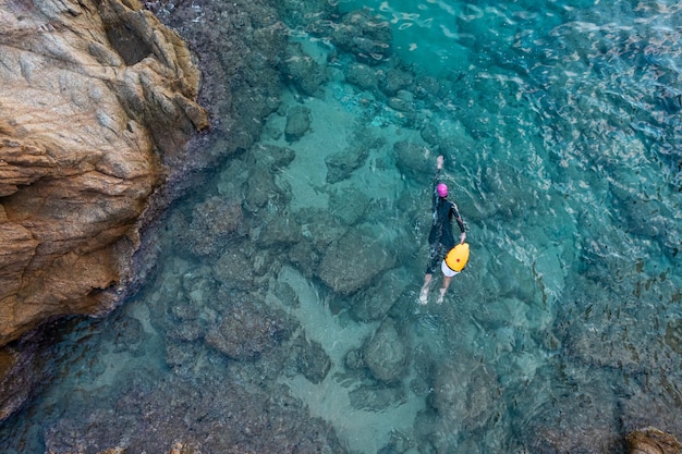 Vista superior aérea desde un dron de un nadador en aguas abiertas con traje de neopreno y boya