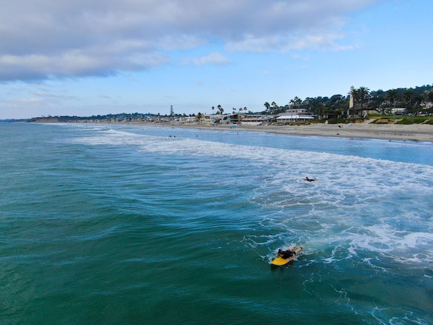 Vista superior aérea de surfistas esperando las olas en agua azul. Playa Del Mar, California, Estados Unidos.