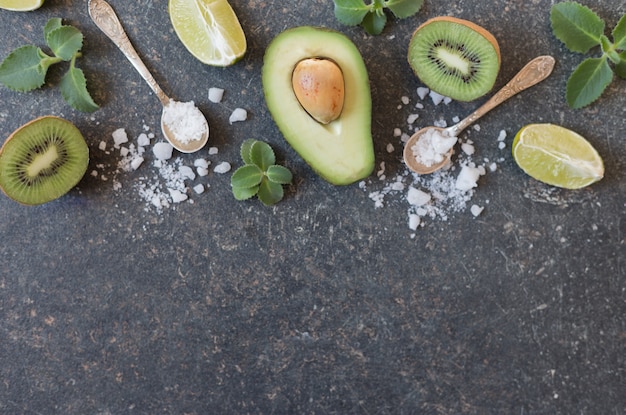 Vista superior de un aguacate con rodajas de limón y kiwi sobre un fondo negro con espacio para texto