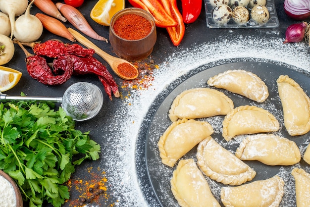 Vista superior de albóndigas crudas en una placa gris con harina alrededor y verduras frescas pimiento rojo