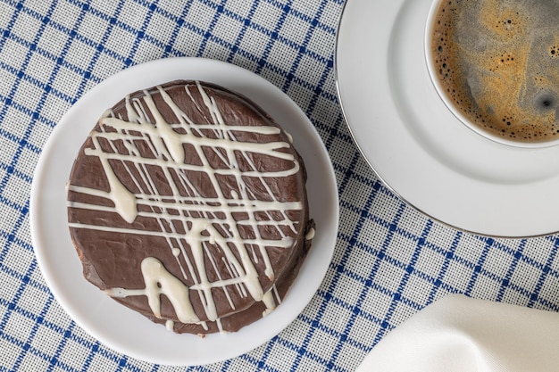 Vista superior del alfajor de chocolate marrón dulce típico en Argentina con una taza de café sobre un mantel a cuadros