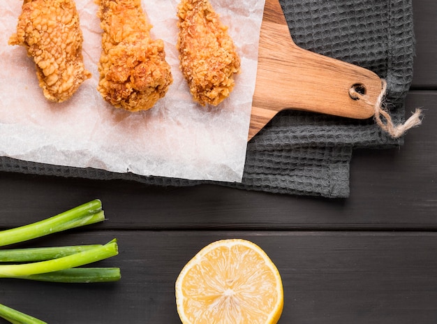 Vista superior de alitas de pollo frito en tabla de cortar con limón y cebolla verde