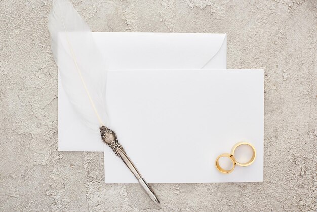 Foto vista superior de los anillos de boda y la pluma de pluma en una tarjeta blanca vacía en una superficie texturizada