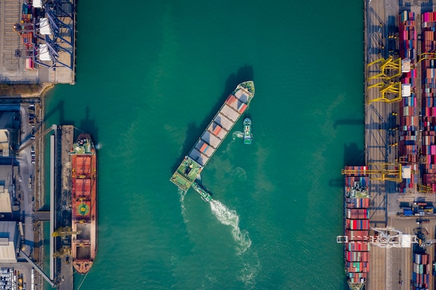 Vista superior de la antena Remolcador empujando el buque portacontenedores al muelle para cargar y descargar el contenedor a través de una grúa para logística