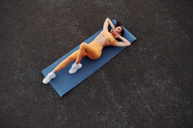 Foto vista superior apoyándose en la alfombra mujer joven en ropa deportiva tiene sesión de fitness al aire libre