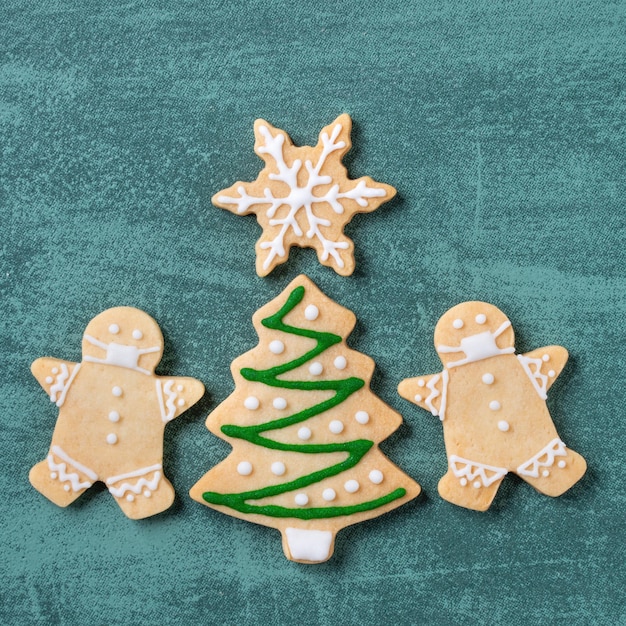 Foto vista superior del árbol de navidad y los cooikes de copos de nieve con el hombre de pan de jengibre con máscara en el fondo de la mesa verde