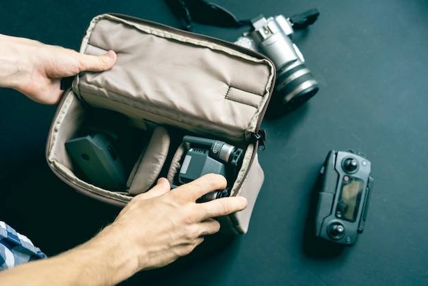 Vista superior de arriba de la mano poner accesorios de la cámara en la bolsa sobre fondo oscuro