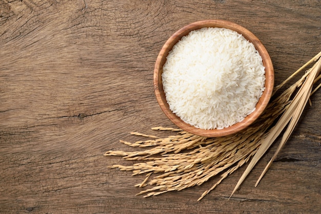 Vista superior del arroz jazmín blanco con espigas de arroz con cáscara sobre fondo de madera